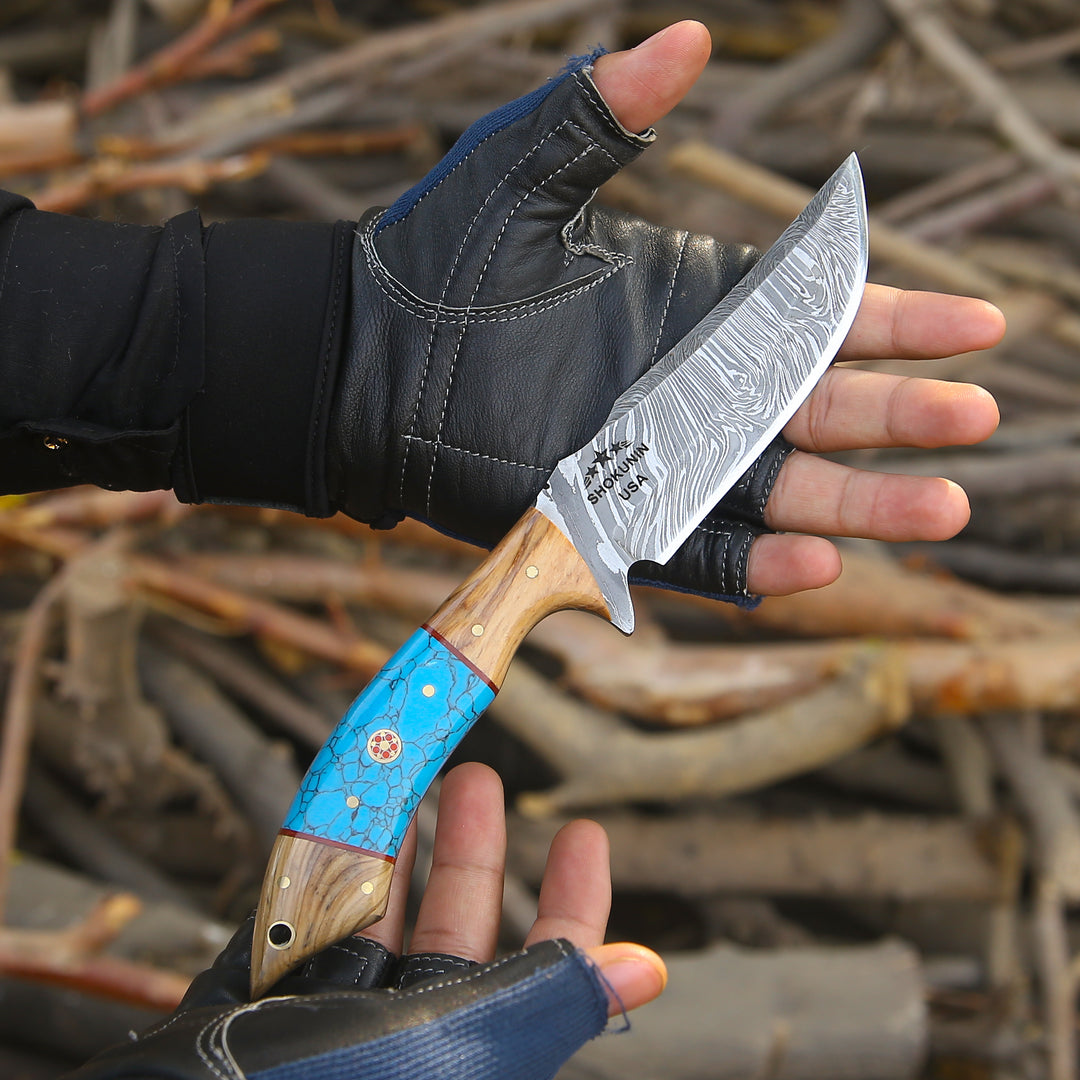 Hand holding a knife with a wooden handle and blue sheath against a blurred natural background