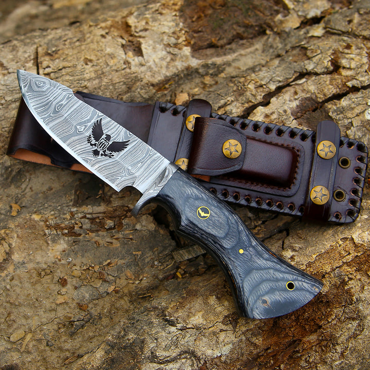 Decorative knife with engraved blade and leather sheath on a wooden surface