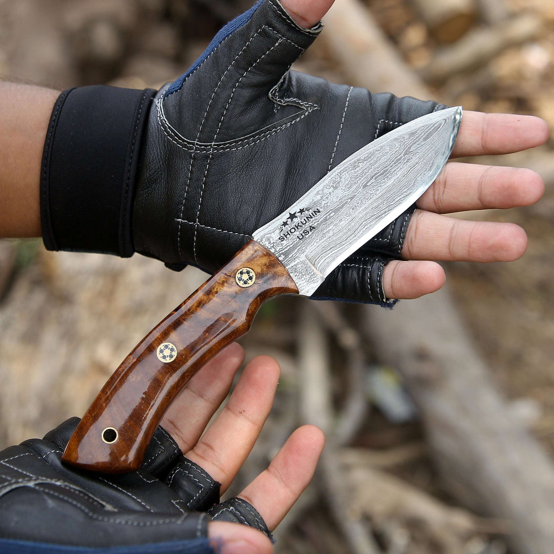 Hand holding a knife with a wooden handle and metal blade, wearing a black glove.
