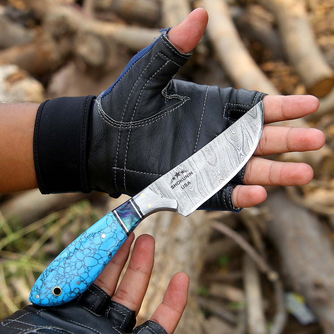 Hand holding a knife with a blue handle and black glove against a natural background
