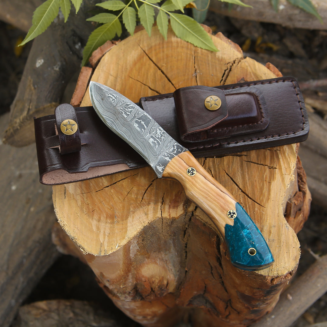 Knife with wooden handle and blue blade in a leather sheath on a wooden log