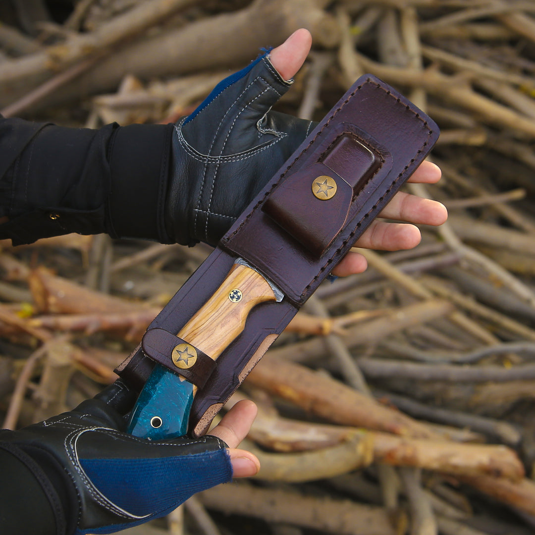 Hand holding a knife with a leather sheath against a natural background