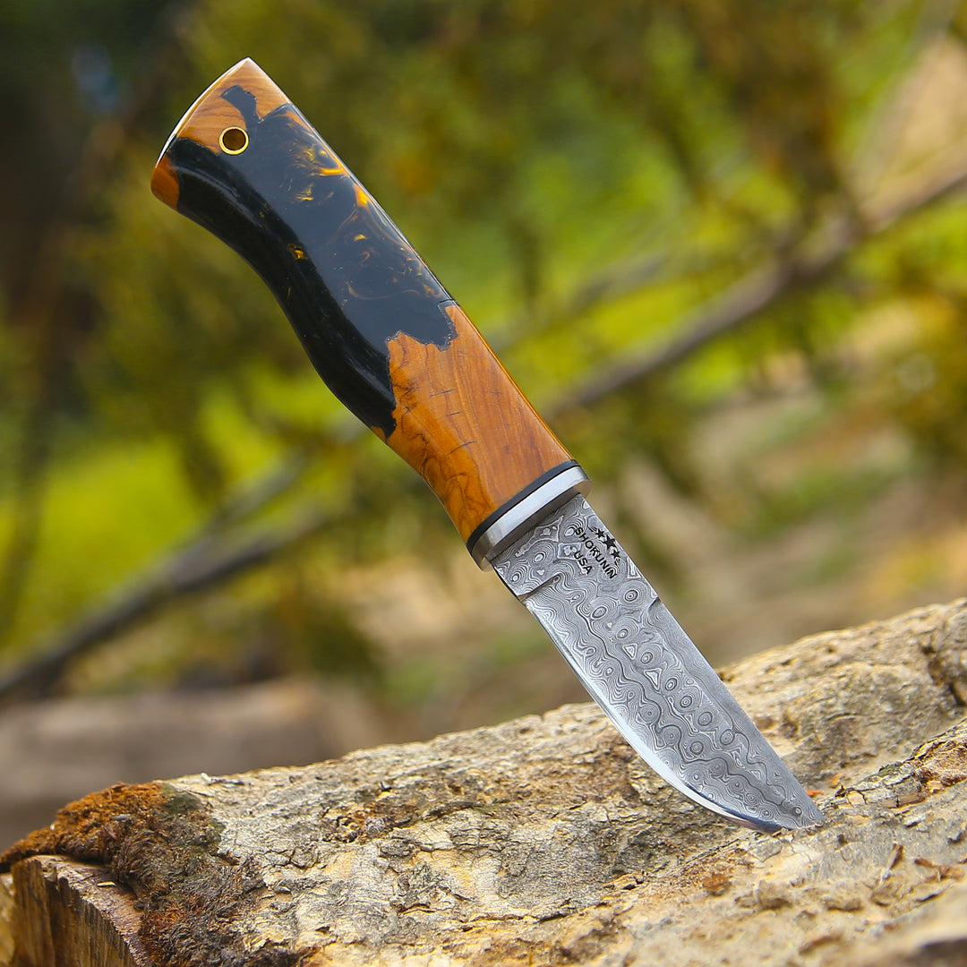 Knife with a decorative blade and wooden handle on a rock with a blurred natural background
