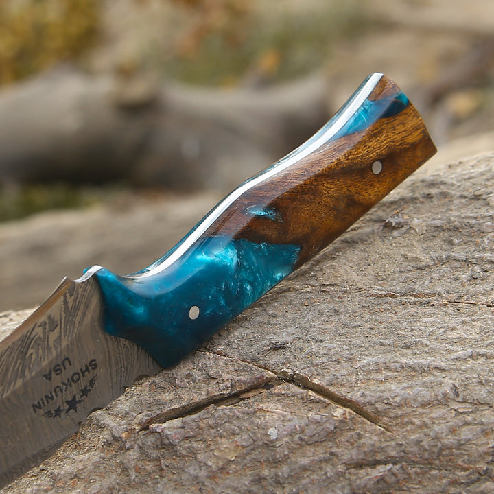 Knife with a wooden handle and blue resin on a stone surface